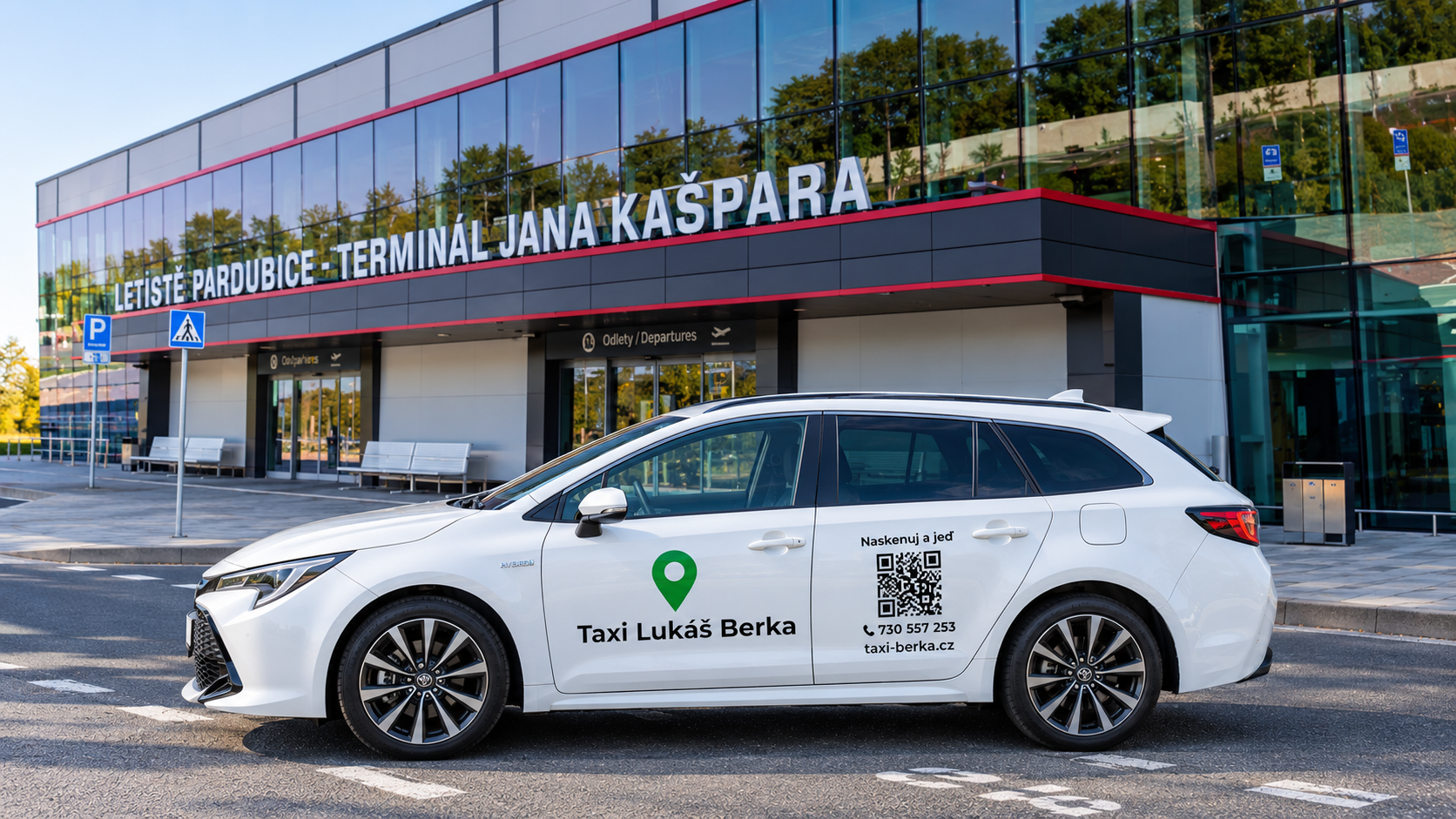 Bílé taxi s logem a QR kódem stojí před letištním terminálem Pardubice, nápis na fasádě.
